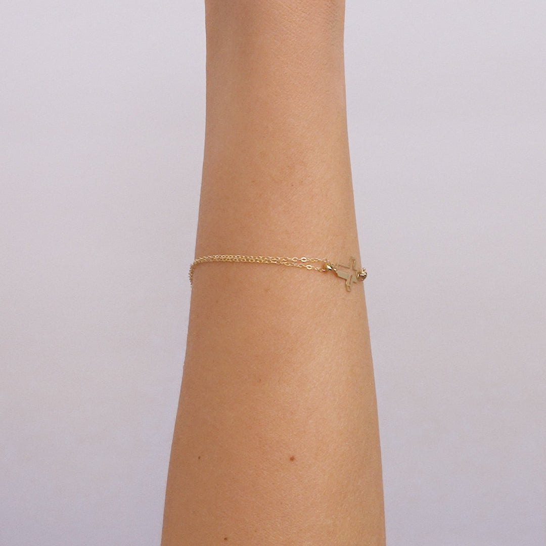 14K solid yellow gold 3D small cross bracelet displayed on a wrist, showcasing its dainty and elegant design.