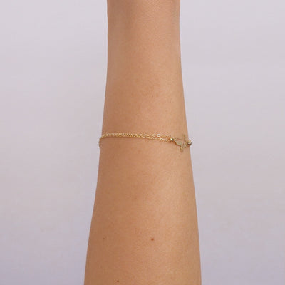 14K solid yellow gold 3D small cross bracelet displayed on a wrist, showcasing its dainty and elegant design.