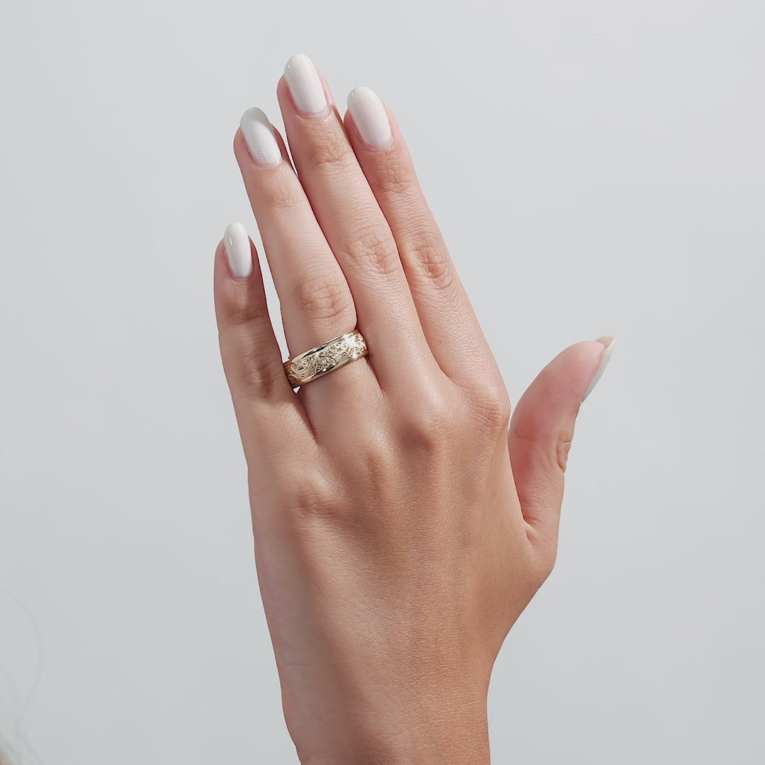 Close-up of a hand wearing a 14K yellow gold hand engraved mens wedding band with a shiny finish.