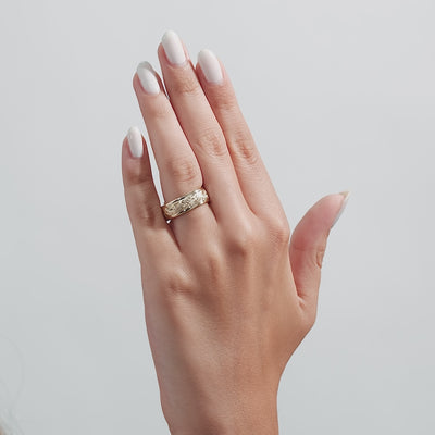 Close-up of a hand wearing a 14K yellow gold hand engraved mens wedding band with a shiny finish.