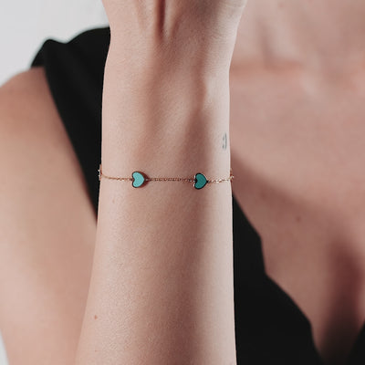 14K yellow gold turquoise heart bracelet worn on wrist, displaying two heart charms and a stylish design.