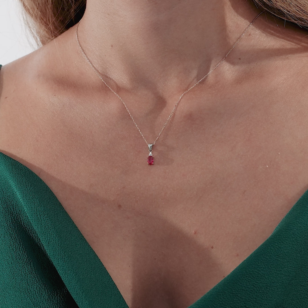 Model wearing a 14K white gold oval ruby and diamond solitaire necklace, showcasing elegance on a textured green dress.