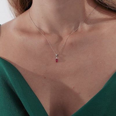 Model wearing a 14K white gold oval ruby and diamond solitaire necklace, showcasing elegance on a textured green dress.