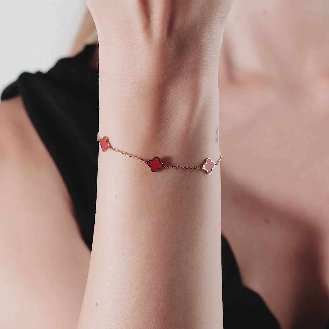 Model wearing a 14K solid yellow gold bracelet featuring red coral four leaf clovers, 7-inch length with a lobster clasp.