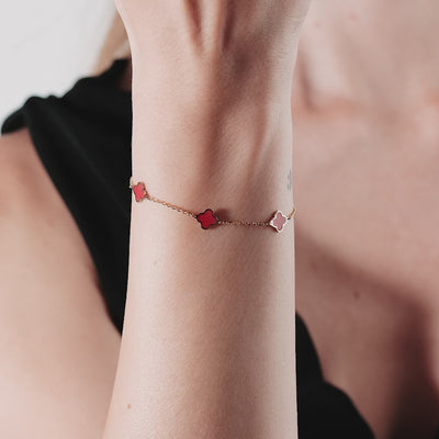 Model wearing a 14K solid yellow gold bracelet featuring red coral four leaf clovers, 7-inch length with a lobster clasp.