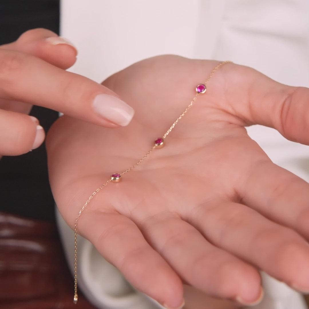 14K yellow gold bracelet with three bezel set lab created rubies displayed on a hand.