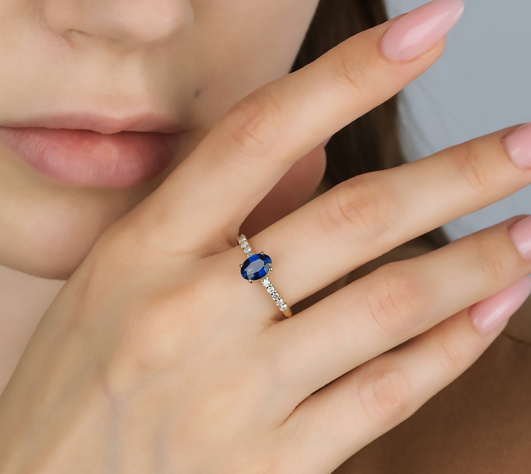 Model showcasing a 14K gold engagement ring with a 1 carat oval sapphire and diamond accents.