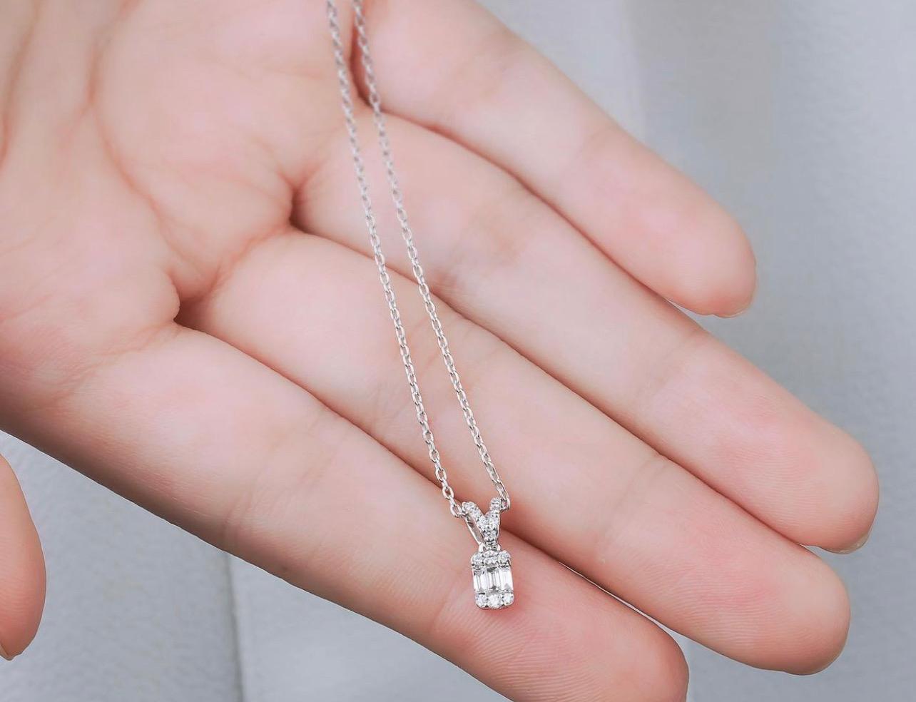 14K gold solitaire baguette diamond necklace held in hand, featuring delicate design and sparkling diamonds.
