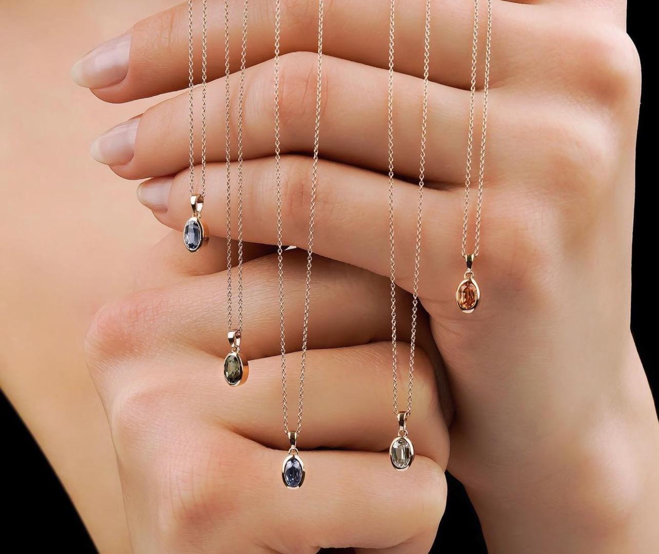 Elegant collection of gemstone pendant necklaces displayed on a hand, showcasing various colors and styles against a black background.