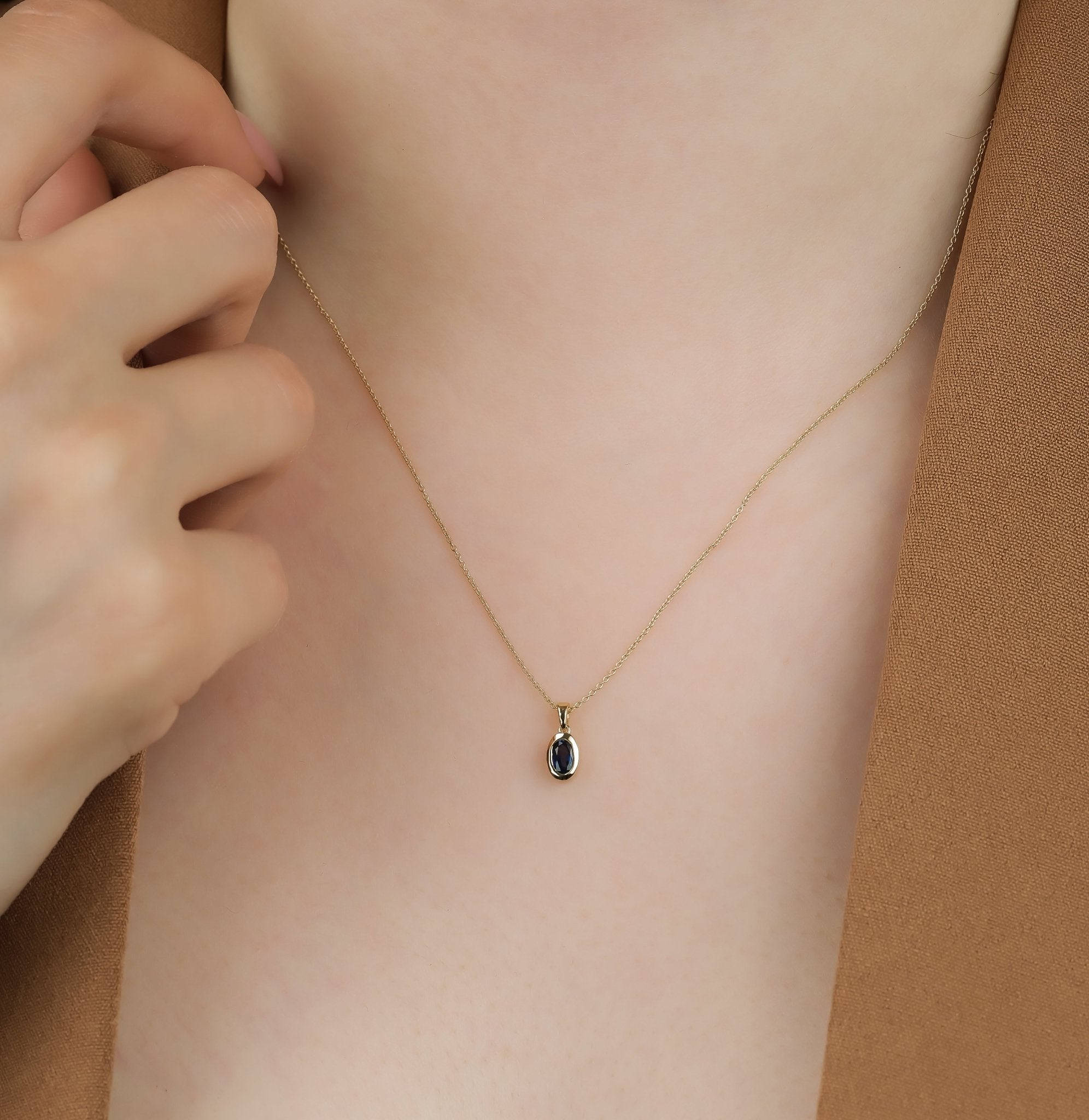 14K gold natural sapphire solitaire necklace worn by a woman, showcasing a delicate pendant on a fine chain.