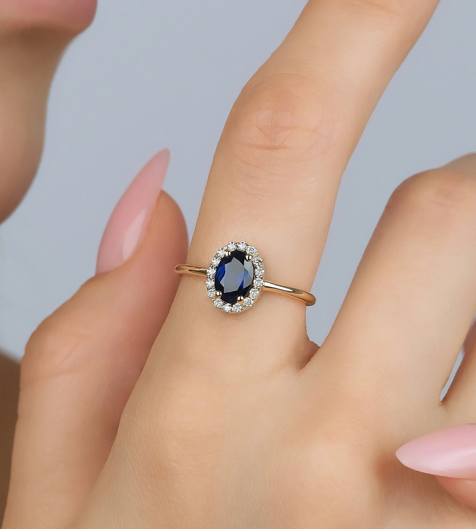 14K gold oval sapphire and diamond engagement ring on a hand, featuring a stunning oval sapphire surrounded by diamonds.