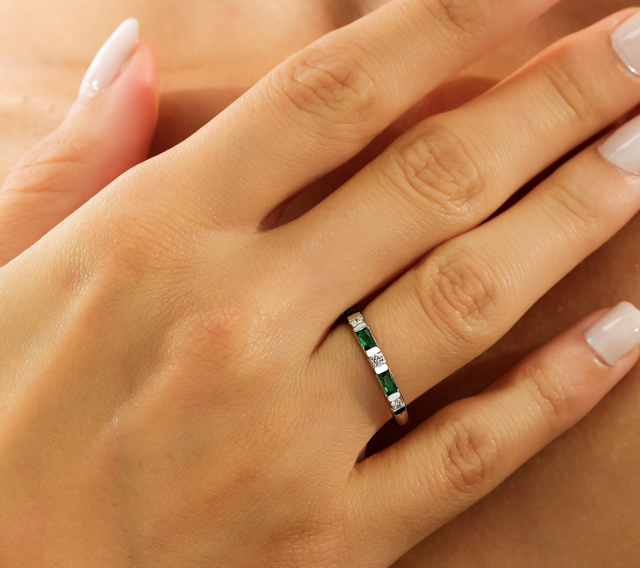 Hand wearing a 14K solid white gold emerald and diamond wedding ring with delicate design.