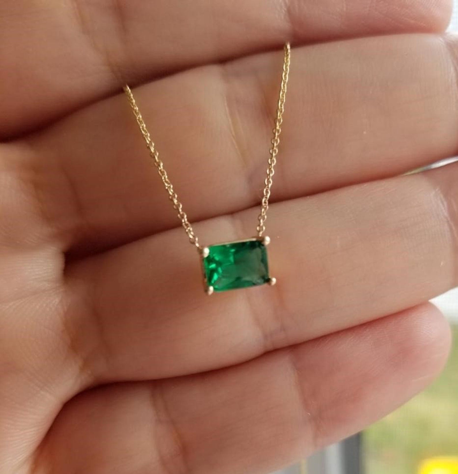 14K White Gold Emerald Cut Solitaire Emerald Necklace held in hand, showcasing a 7x5mm emerald pendant.