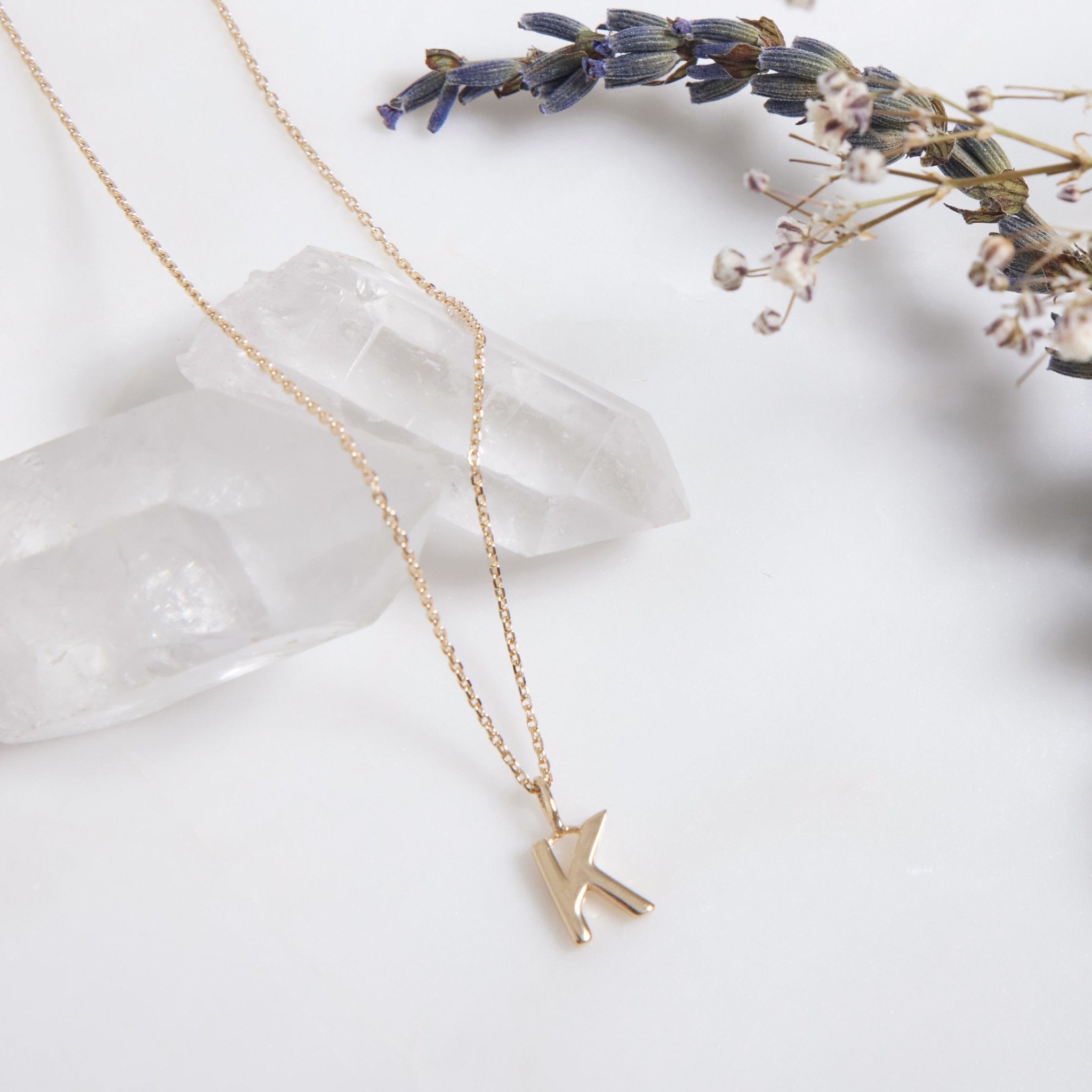 14K solid white gold initial necklace featuring the letter K, on a delicate chain with crystals and flowers as background.