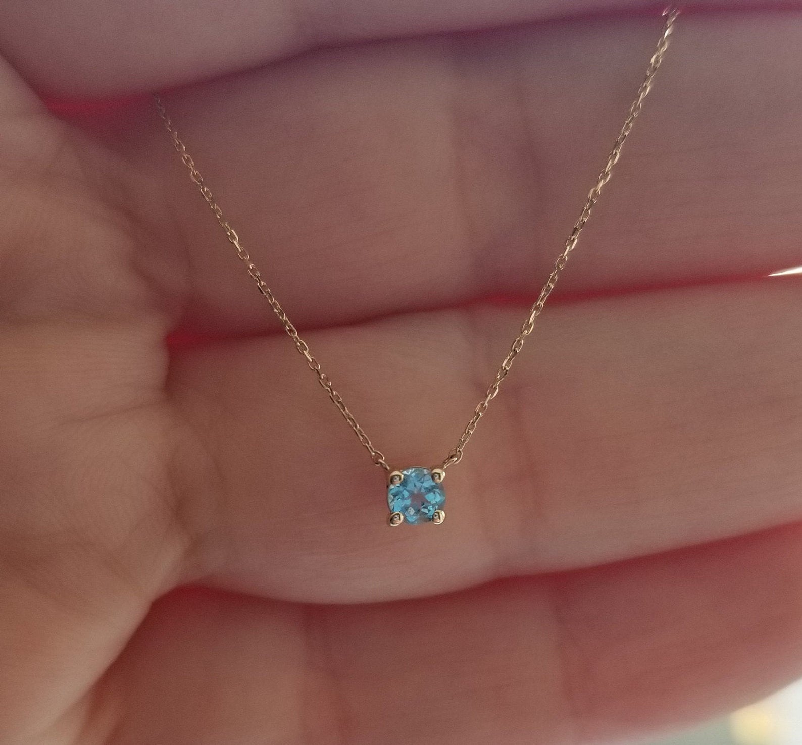 14K yellow gold 5mm prong setting aquamarine solitaire necklace held in hand, showcasing its delicate design.