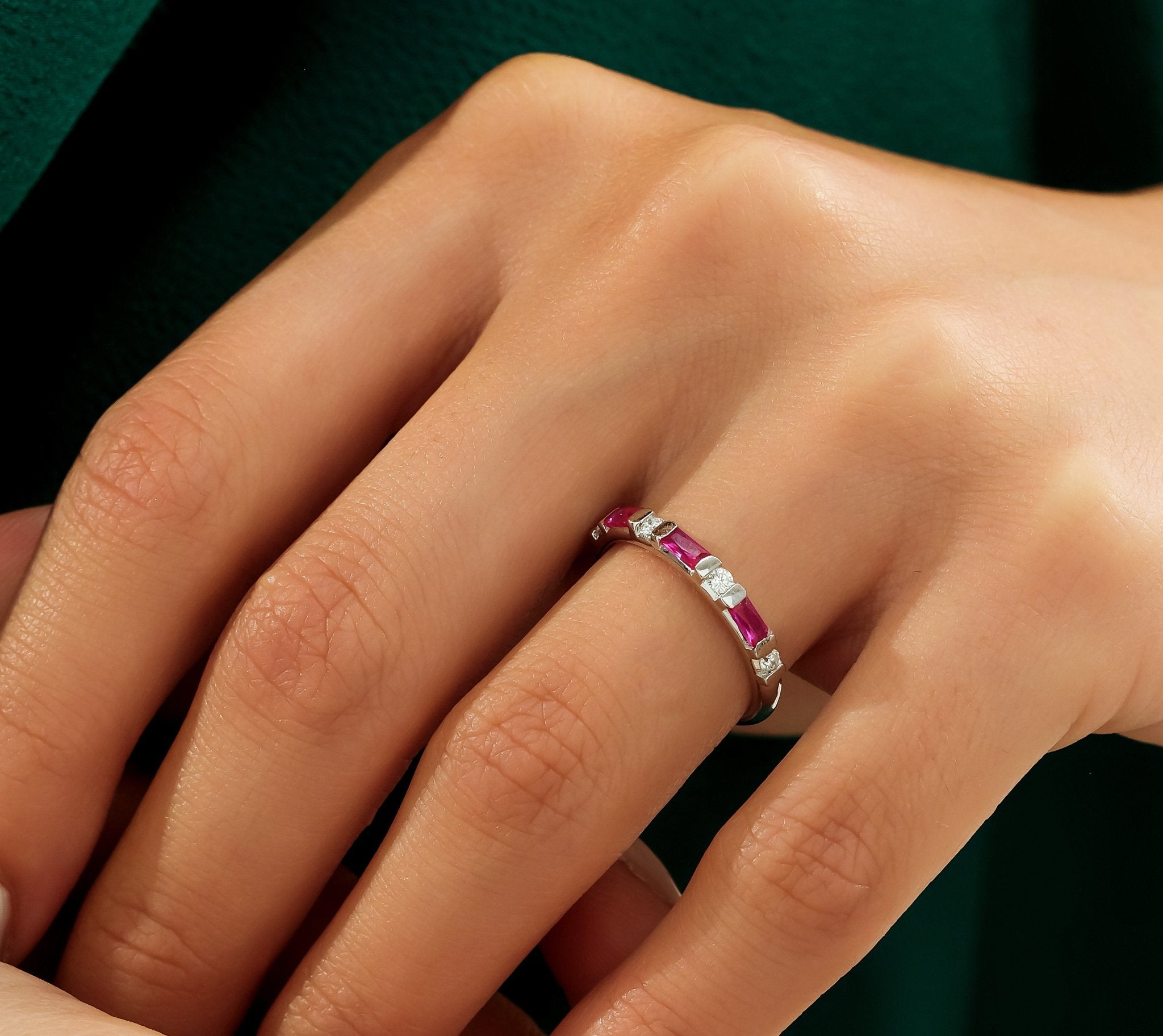 Close-up of a hand wearing a 14K solid white gold ruby and diamond wedding ring with three rubies and two round diamonds.