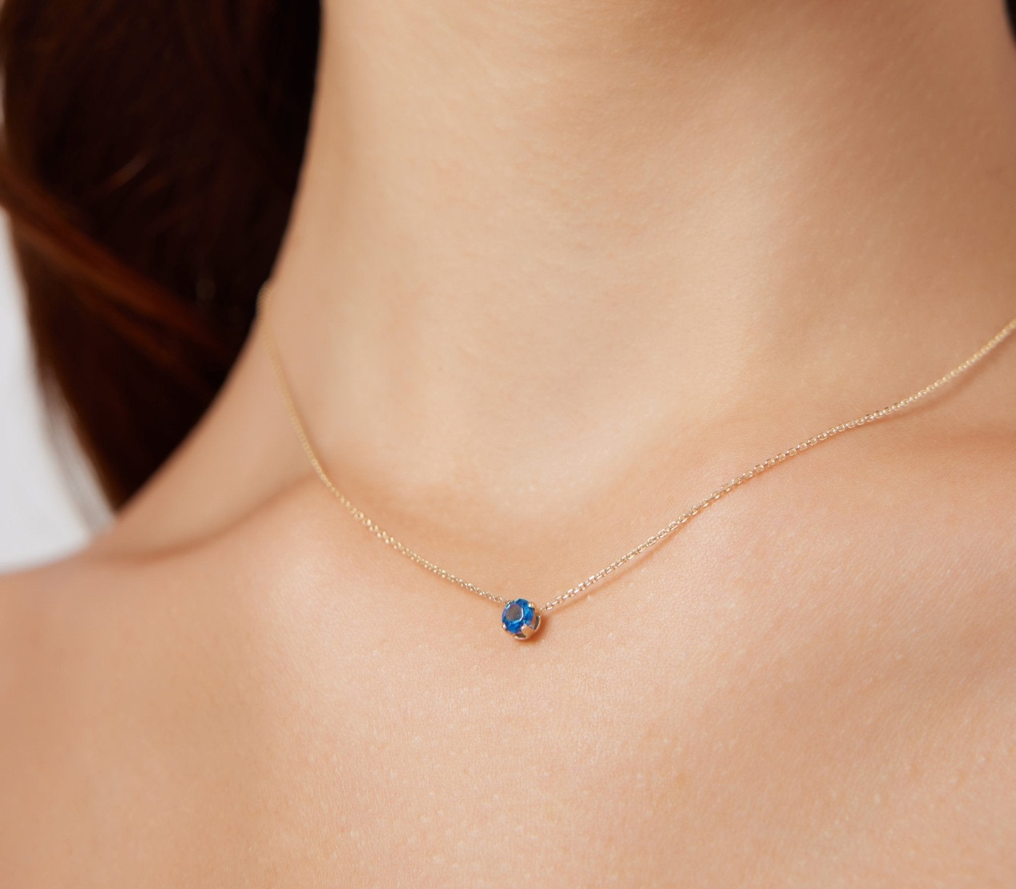 Dainty 14K white gold minimalist prong setting sapphire solitaire necklace worn on neck.