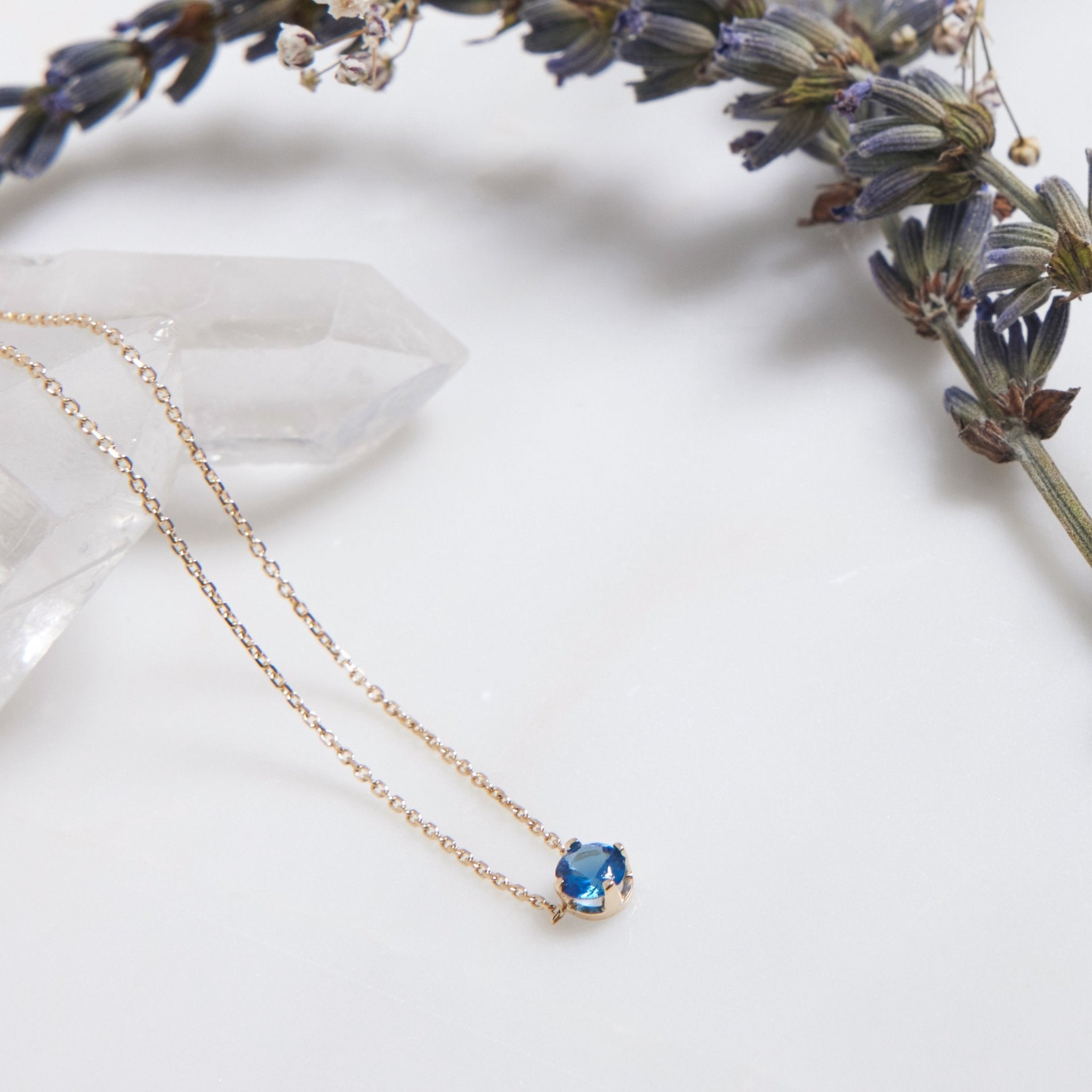 14K white gold 5mm prong setting minimalist sapphire solitaire necklace on marble with lavender.