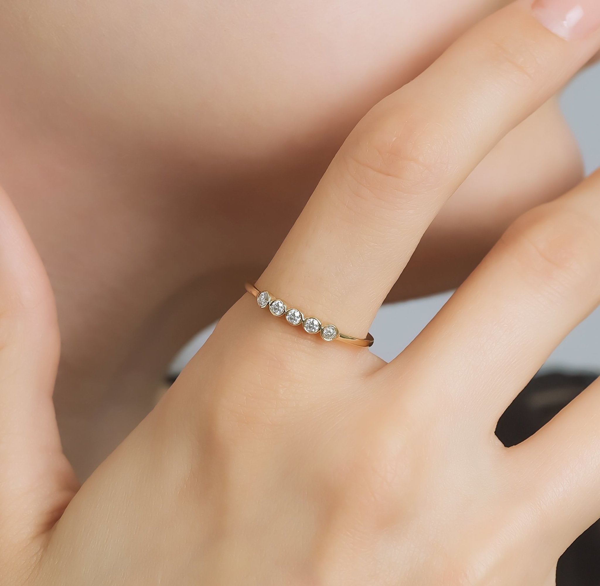 Minimalist 14K yellow gold bezel set diamond wedding ring worn on a hand, featuring five round diamonds.