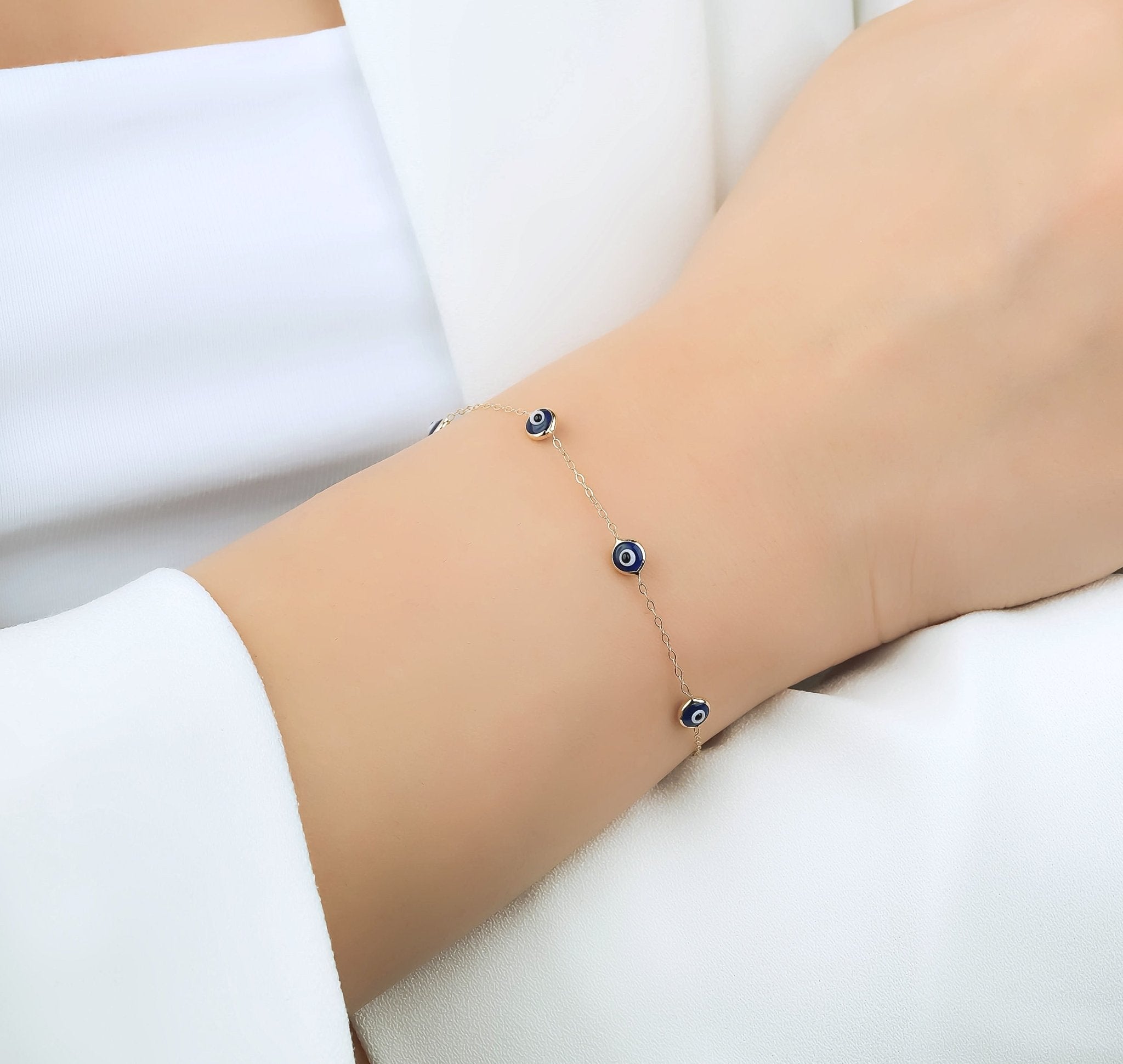 Dainty 14K solid yellow gold evil eye bracelet worn on wrist, featuring three blue evil eye charms.