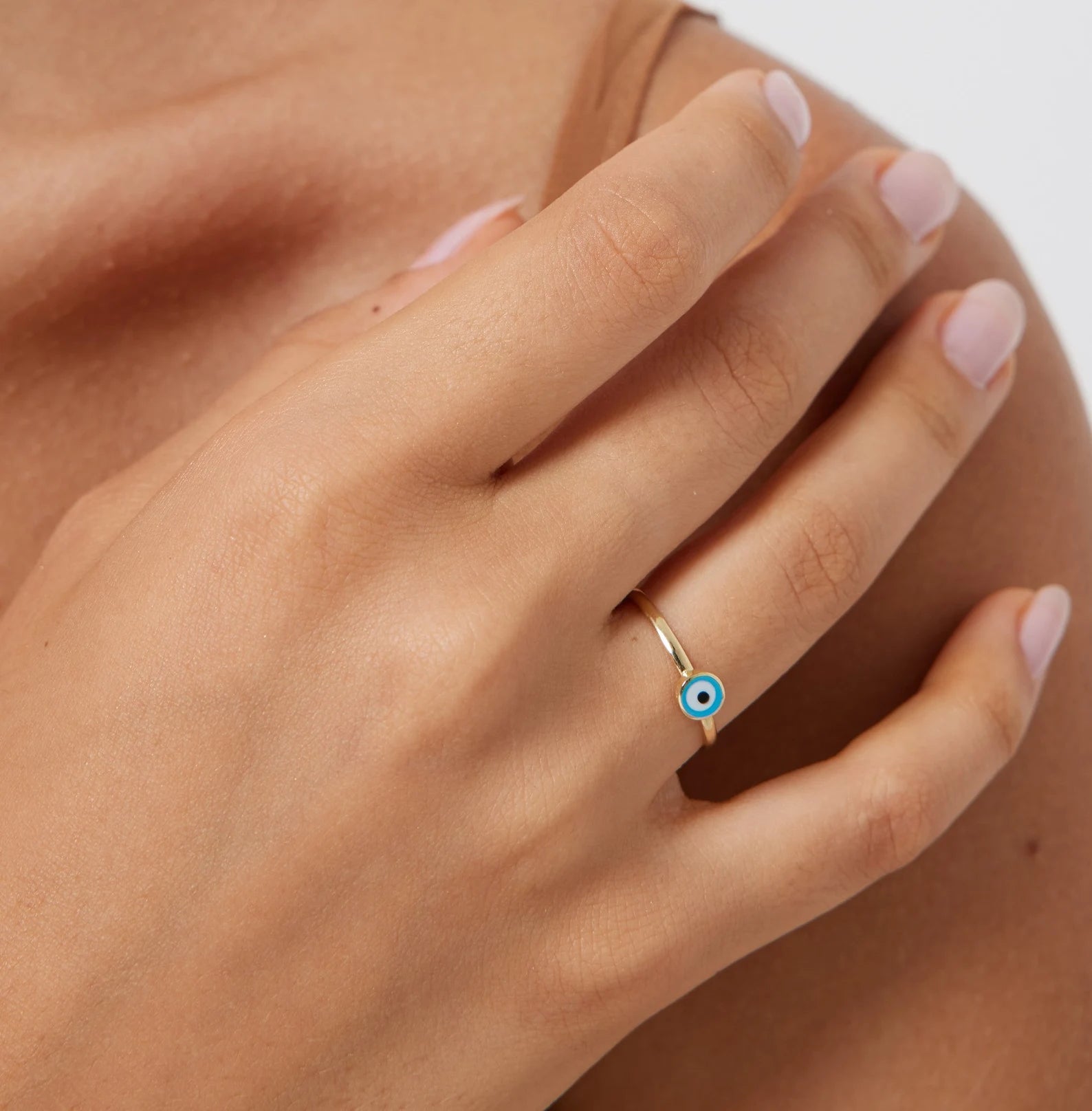 Close-up of a hand wearing a 14K solid yellow gold minimalist evil eye ring, showcasing its delicate design and blue eye detail.