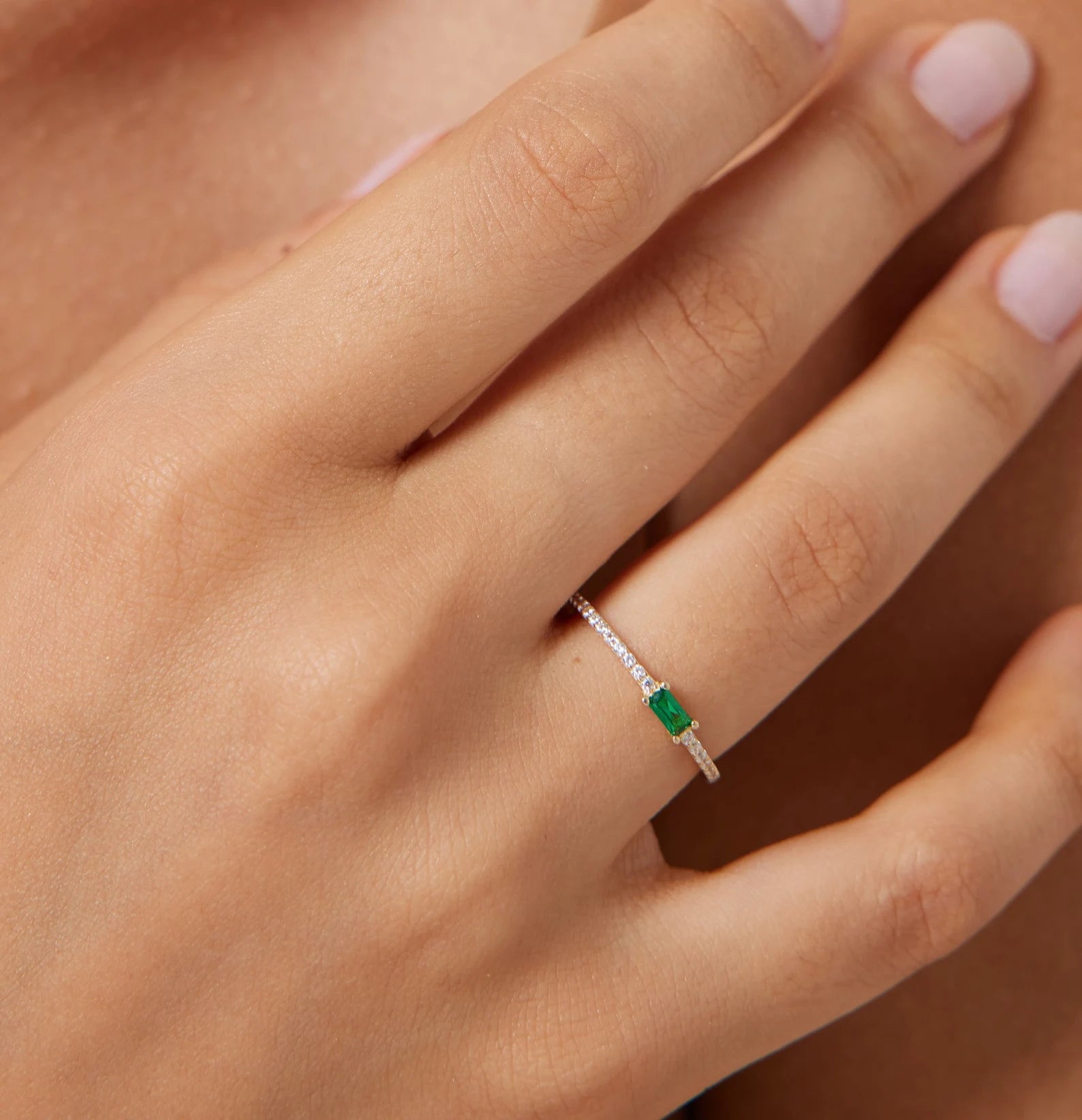 14K yellow gold minimalist emerald and diamond wedding ring on a hand, showcasing its elegant design and emerald stone.