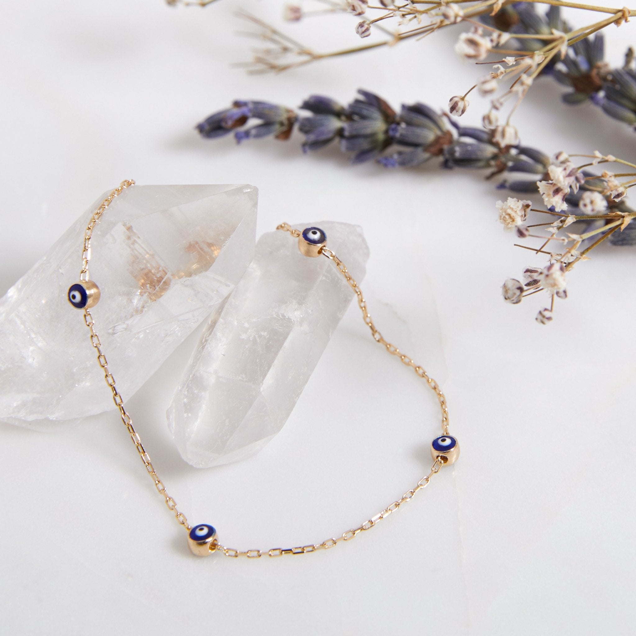 14K solid yellow gold minimalist evil eye bracelet displayed on crystals and lavender flowers.