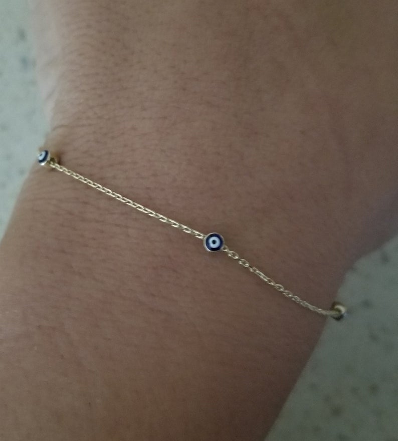 Dainty 14K Solid Yellow Gold minimalist evil eye bracelet worn on wrist, featuring small blue evil eye charms.