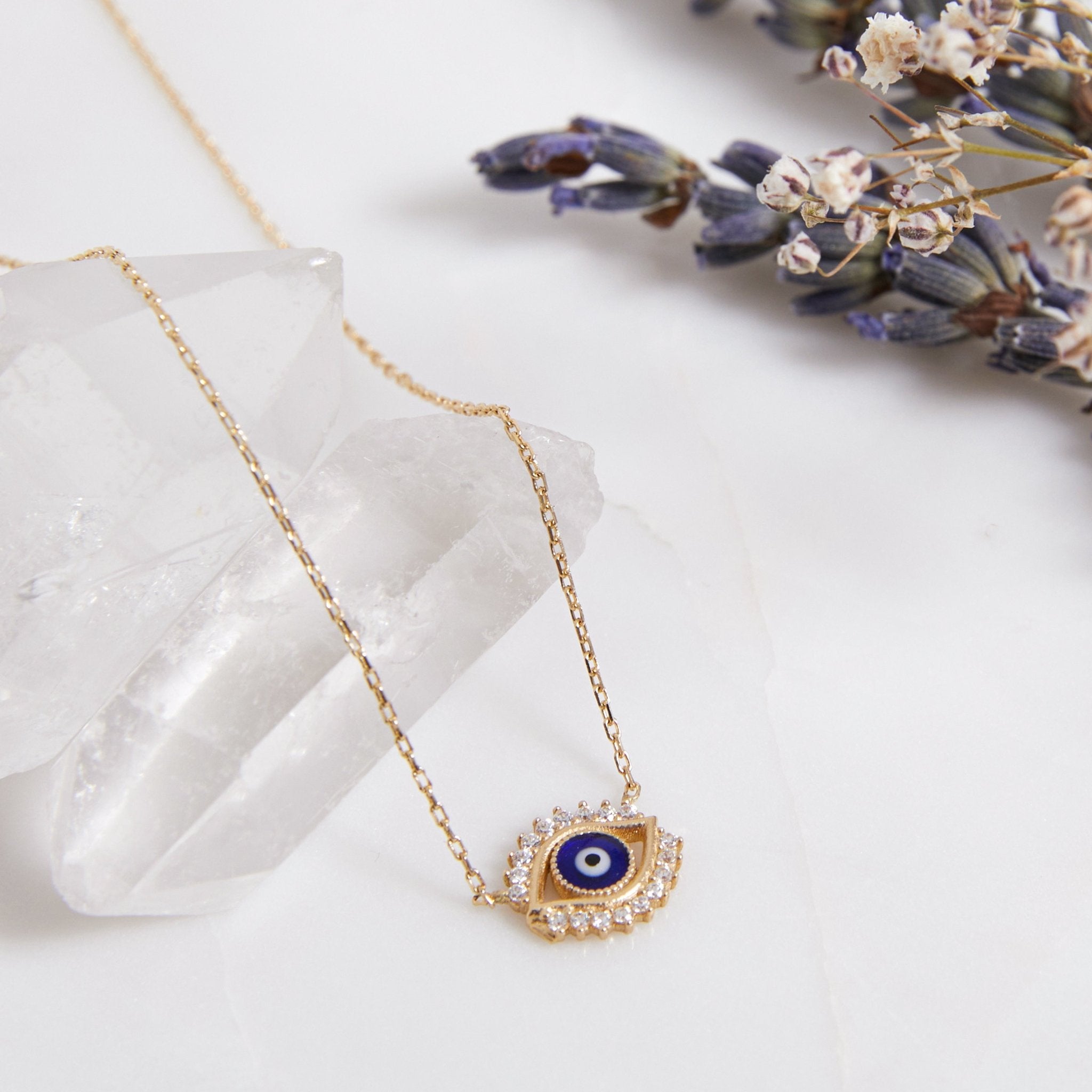 Minimalist 14K solid yellow gold evil eye necklace with CZ, displayed on quartz crystal with dried flowers.