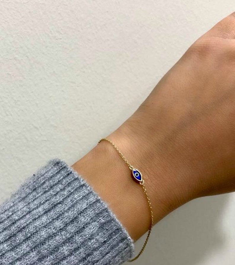 14K solid yellow gold minimalist evil eye bracelet on wrist, featuring a dark blue eye design, perfect for everyday wear.