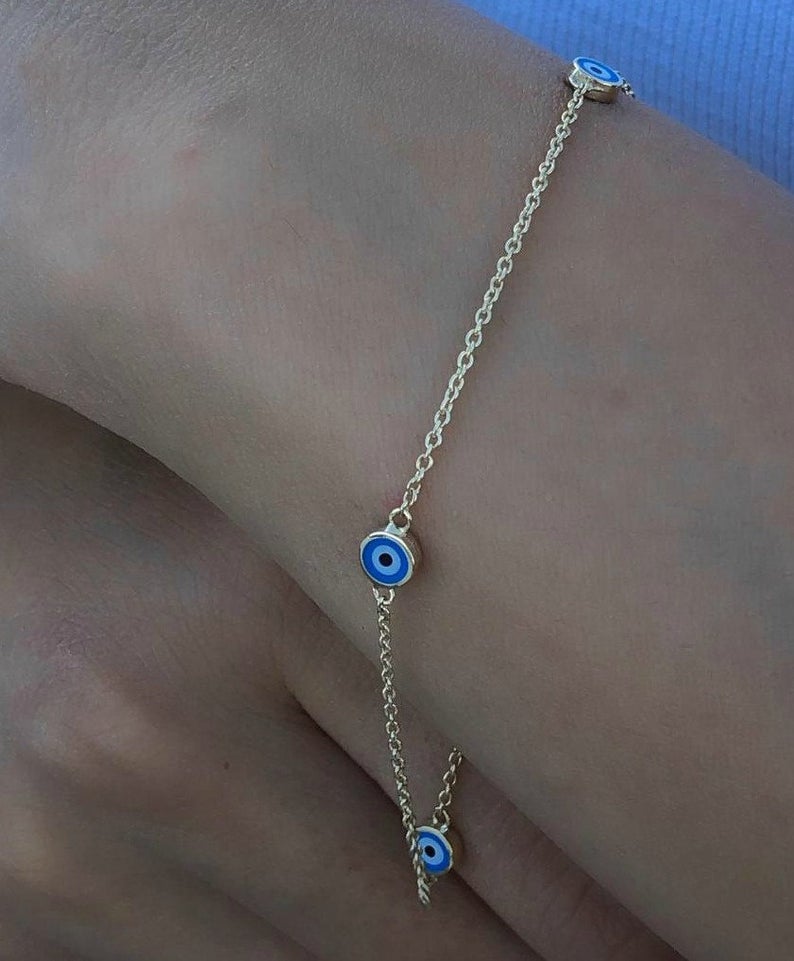 14K solid yellow gold minimalist evil eye bracelet worn on a wrist, featuring blue and white evil eye charms.