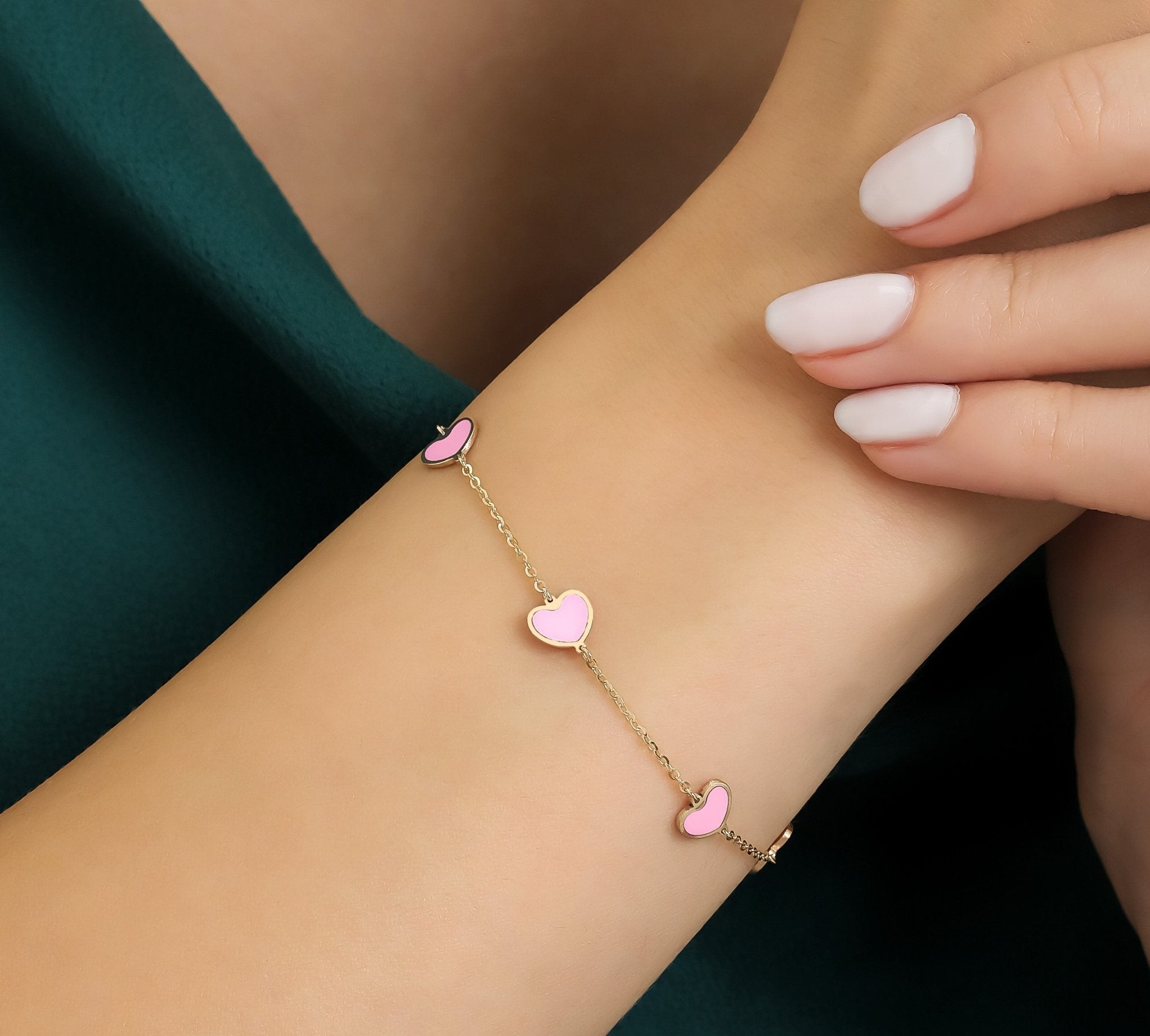14K yellow gold pink heart station bracelet on a wrist, featuring five pink hearts and delicate chain.