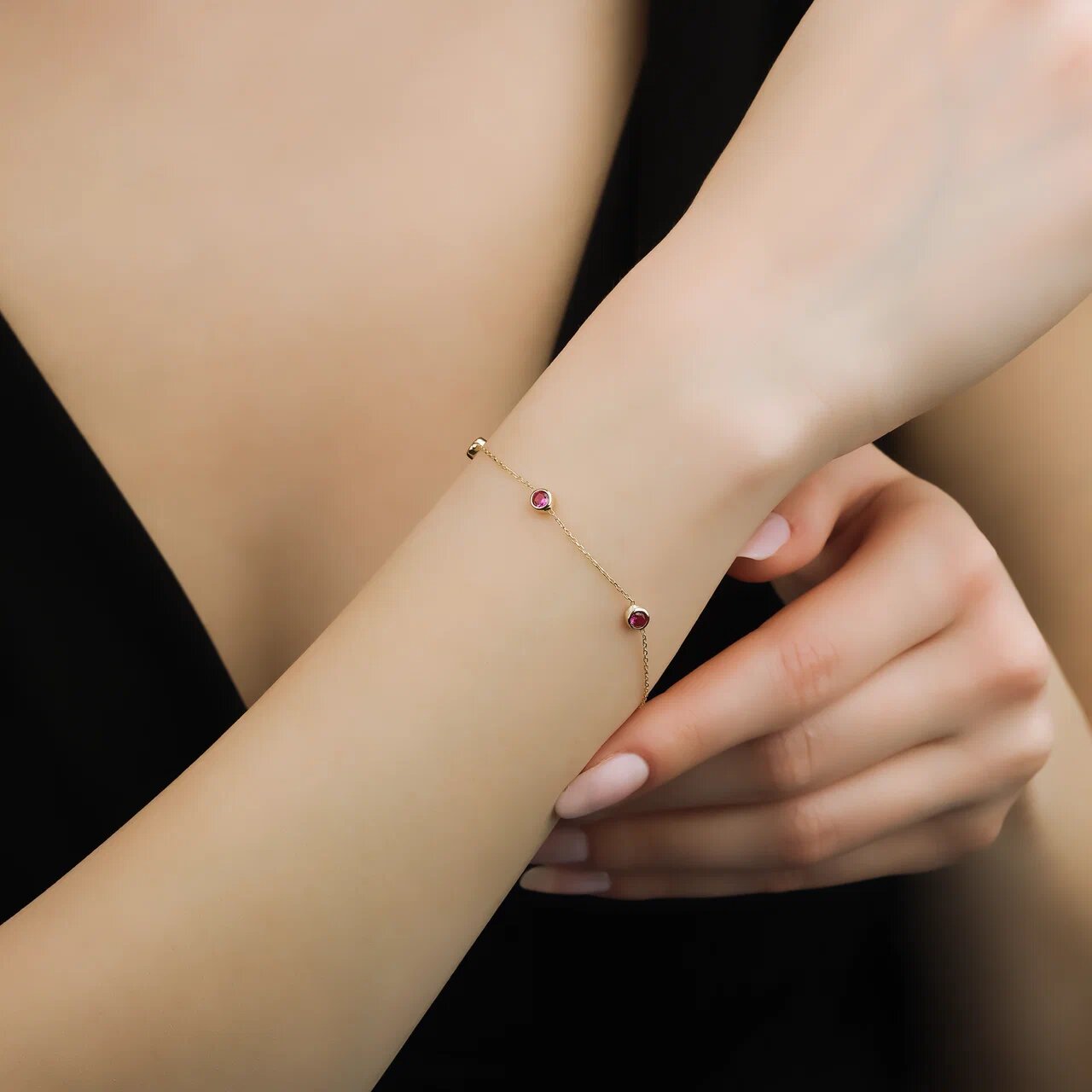 Dainty 14K yellow gold bracelet with three bezel-set lab-created rubies worn on a woman's wrist.