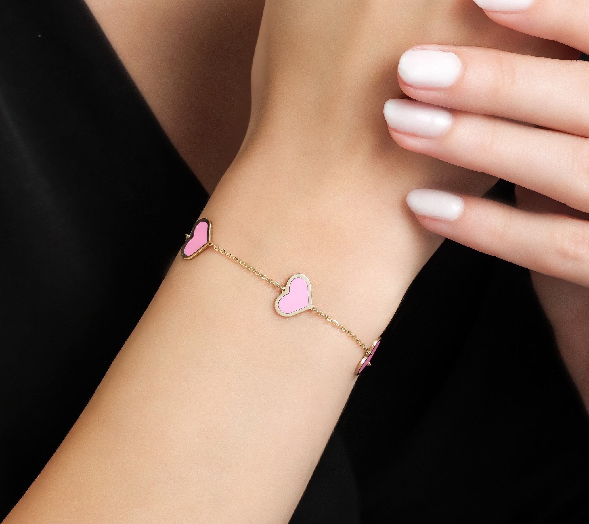 14K solid yellow gold bracelet featuring five pink heart stations on a woman's wrist, elegantly displayed.