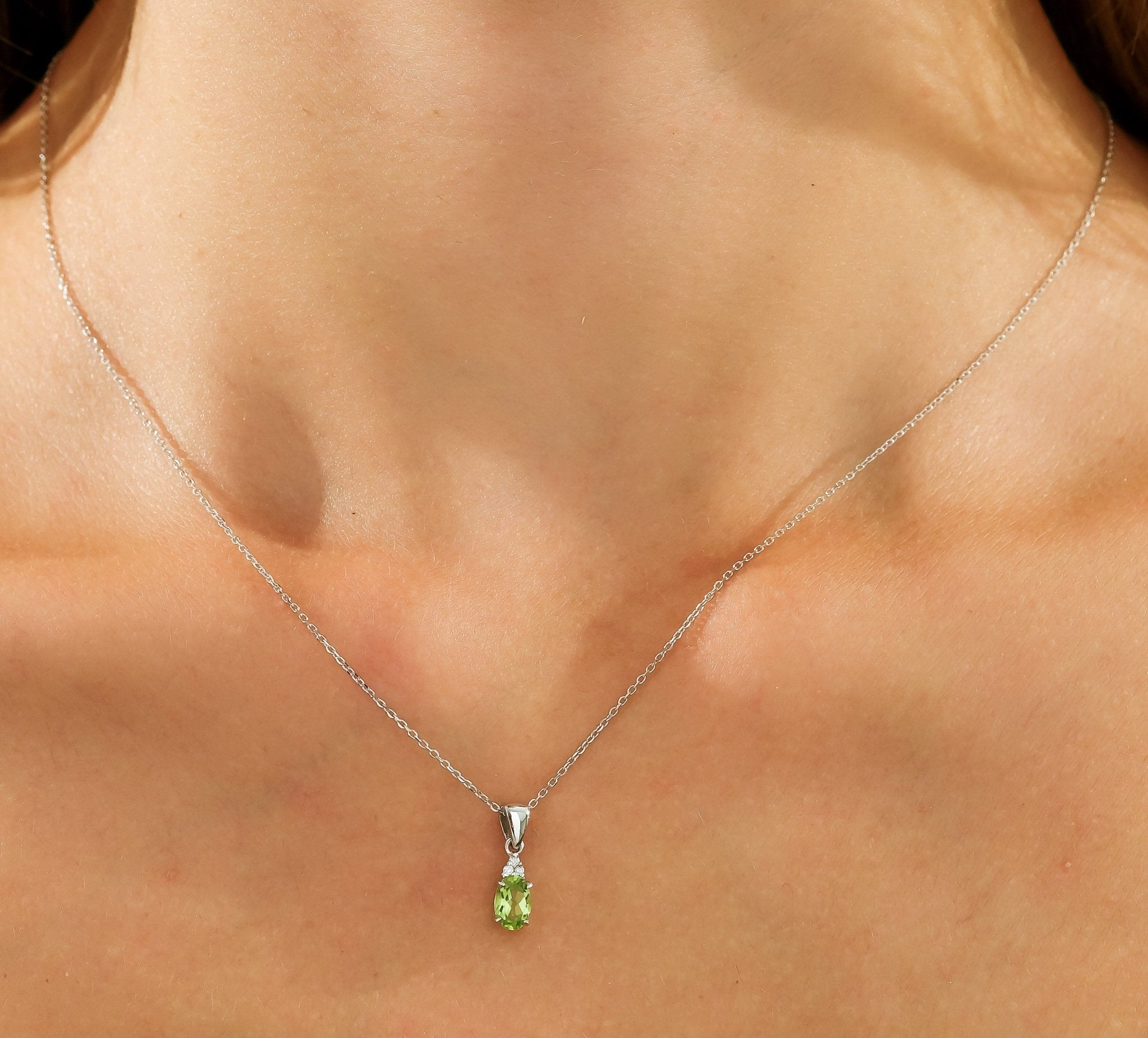 Dainty silver necklace featuring a pear-shaped green gemstone pendant on a model's neck.