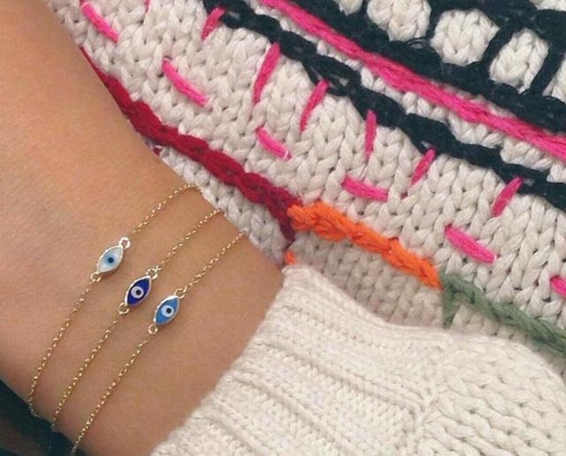 14K yellow gold minimalist evil eye bracelet with blue and white enamel against a cozy knitted background.