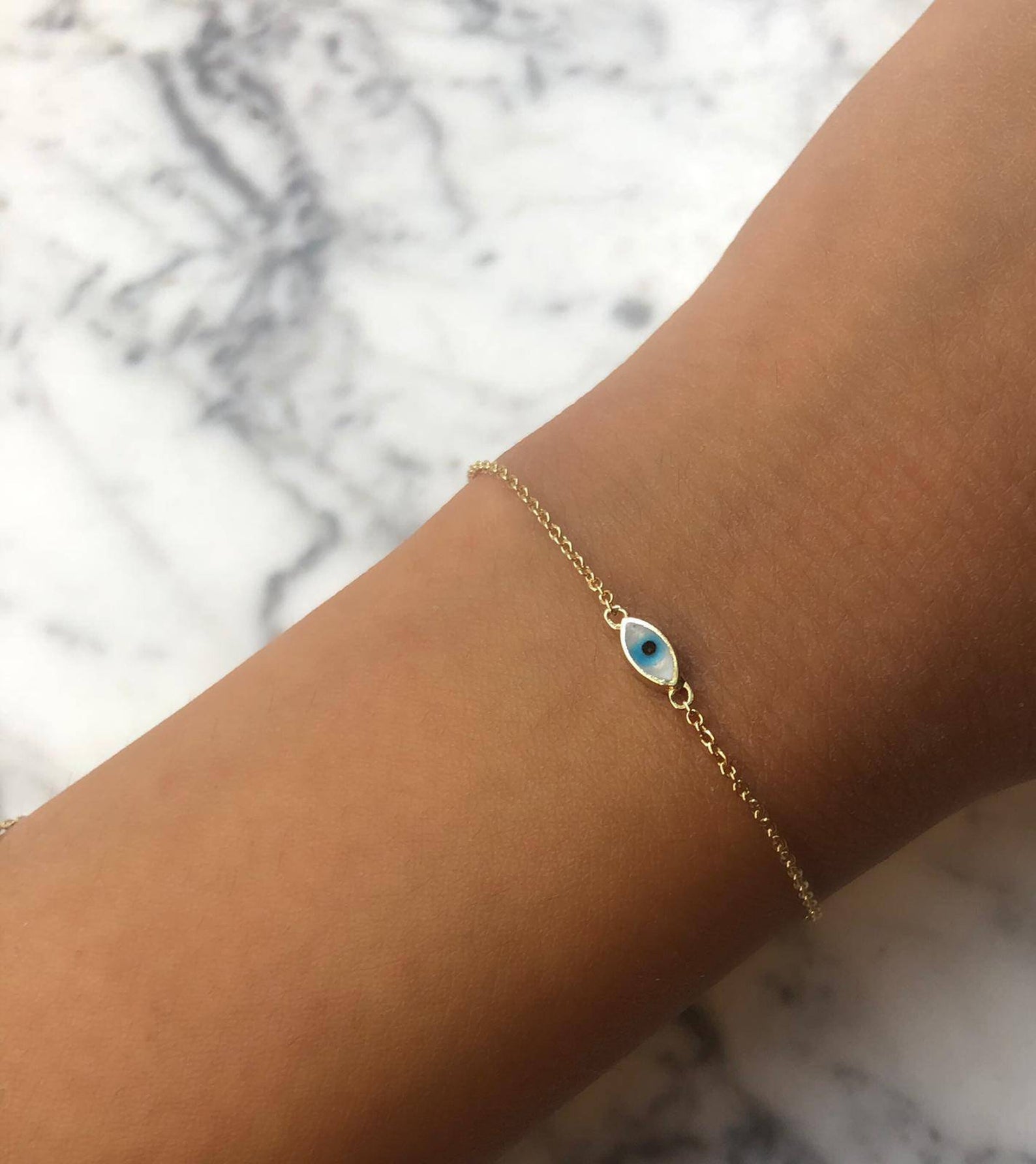 14K yellow gold minimalist evil eye bracelet with white and blue enamel on a wrist, perfect for everyday wear.