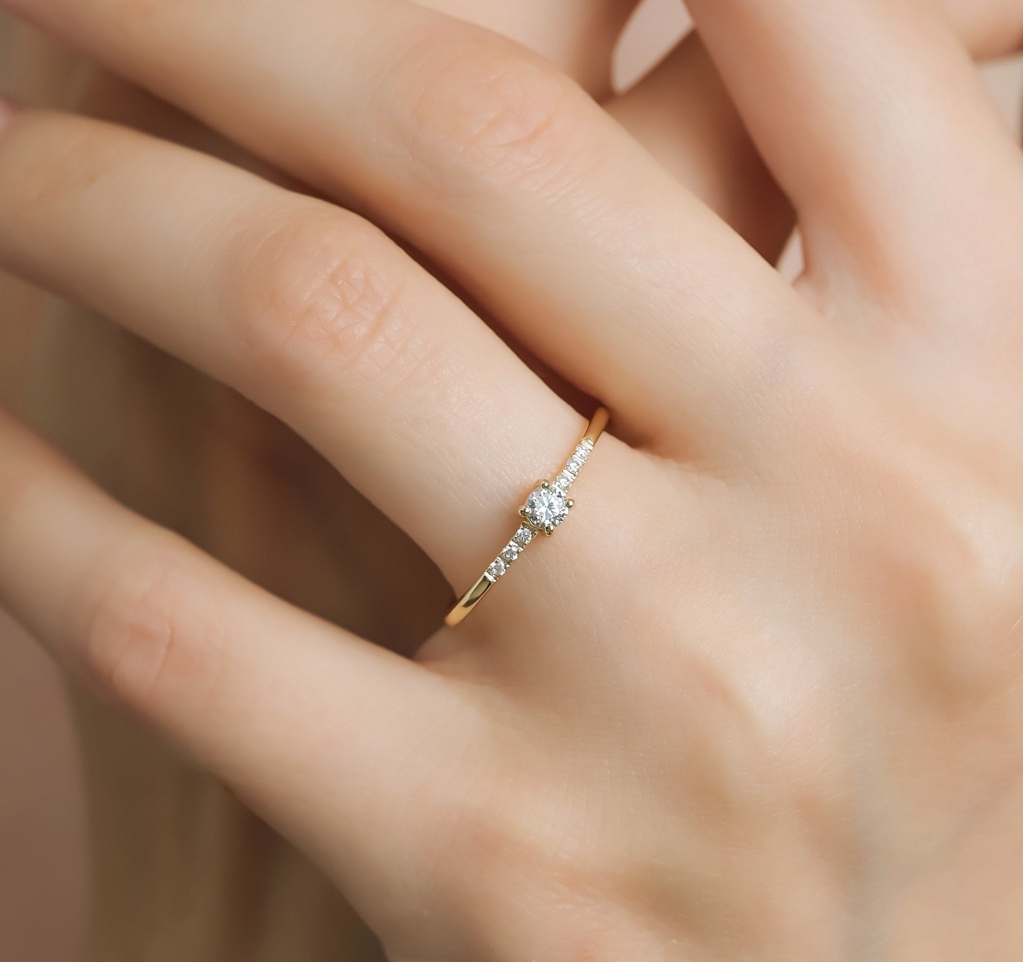14K yellow gold minimalist solitaire diamond engagement ring on a hand, featuring a 3mm center diamond and delicate band.