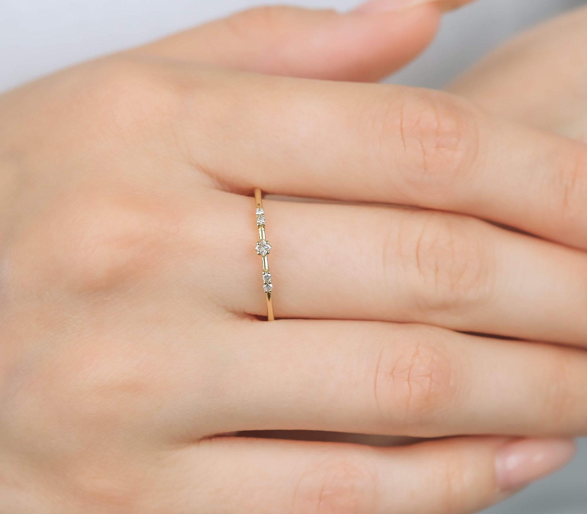 14K yellow gold minimalist women's diamond ring with princess cut center and four round diamonds on a hand.