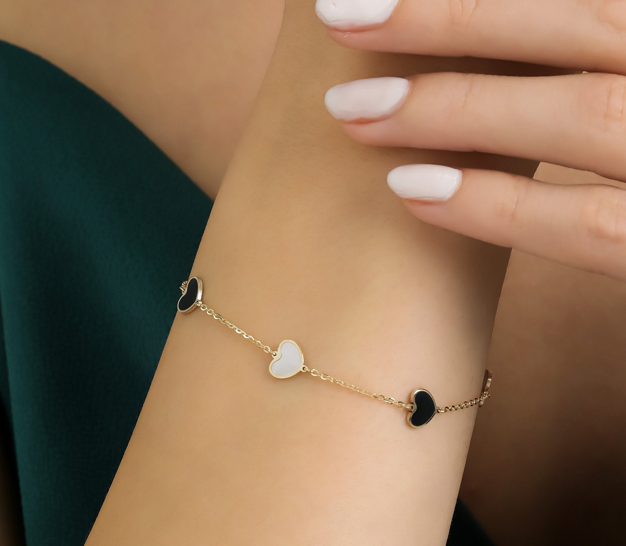 14K yellow gold bracelet featuring black onyx and mother of pearl hearts, elegantly worn on a model's wrist.