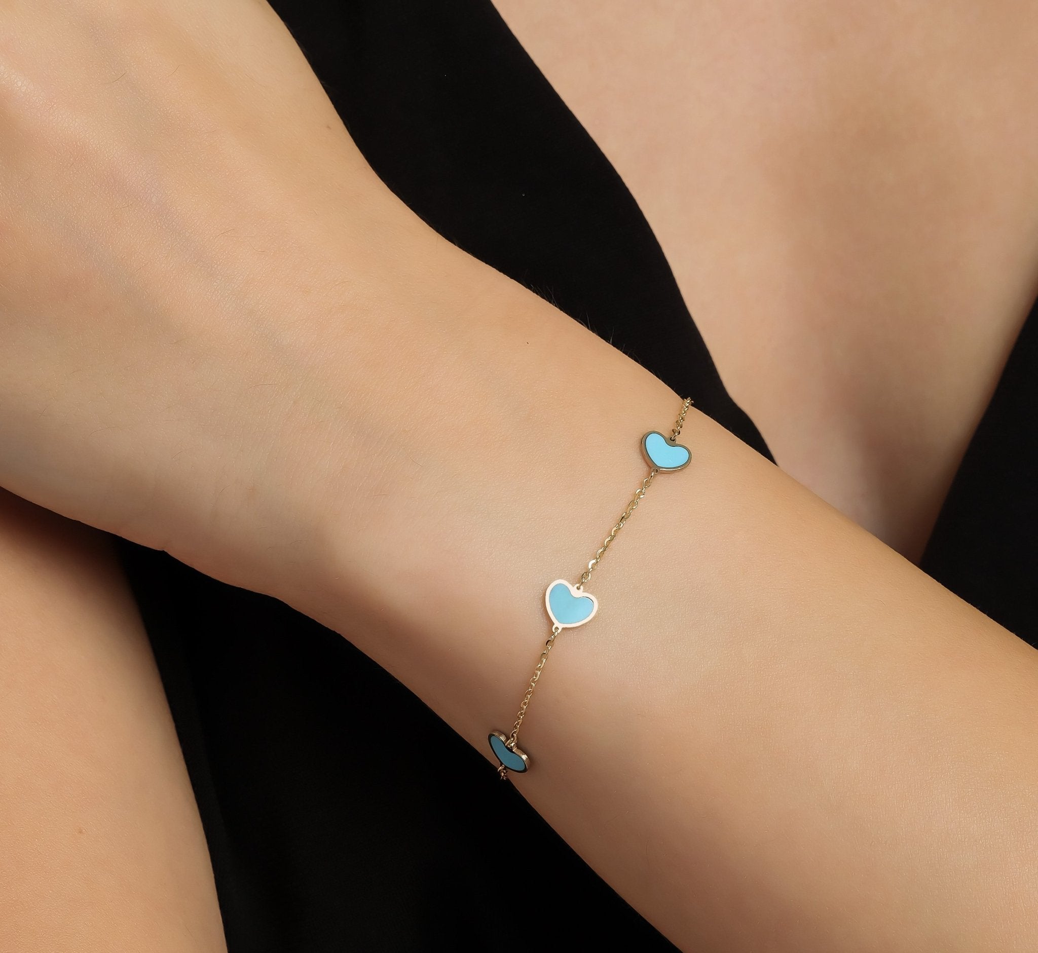 14K yellow gold minimalist turquoise heart bracelet worn on wrist, featuring five heart stations.