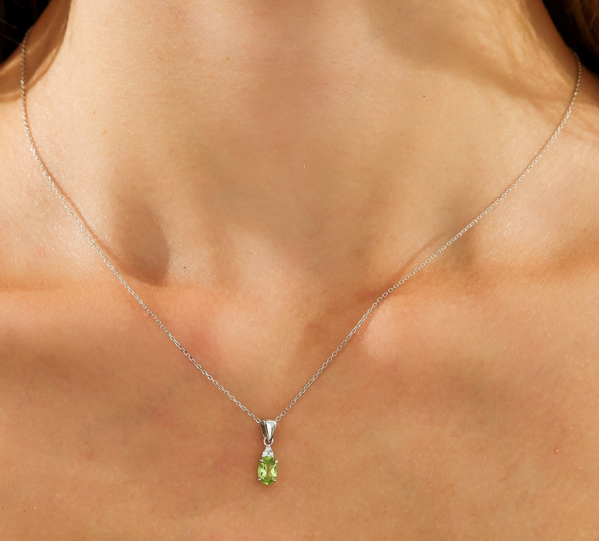 Woman wearing a delicate 14K white gold necklace with an oval green gemstone pendant.