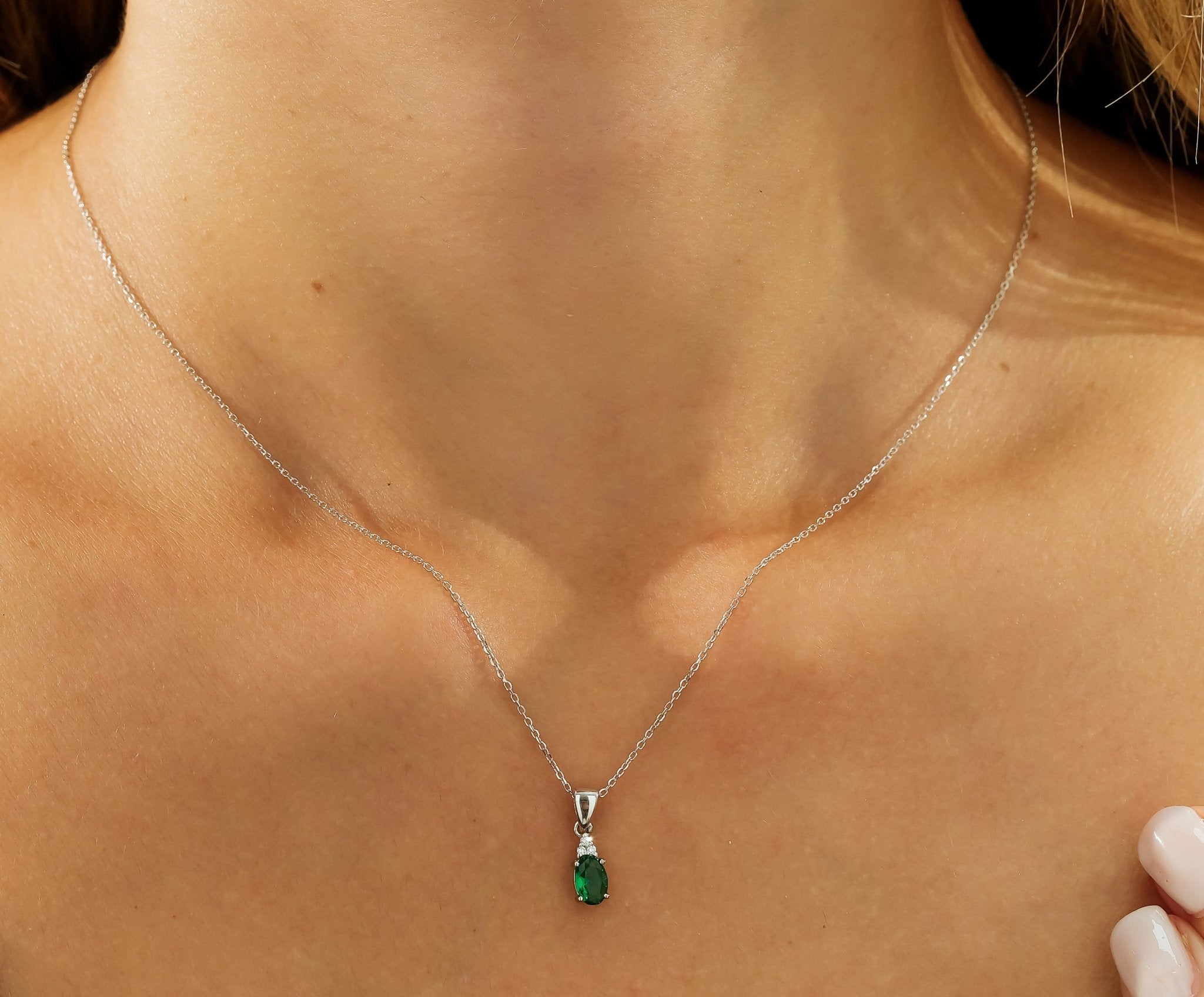 14K white gold oval emerald and diamond solitaire necklace worn on a model's neck, showcasing elegance and sophistication.