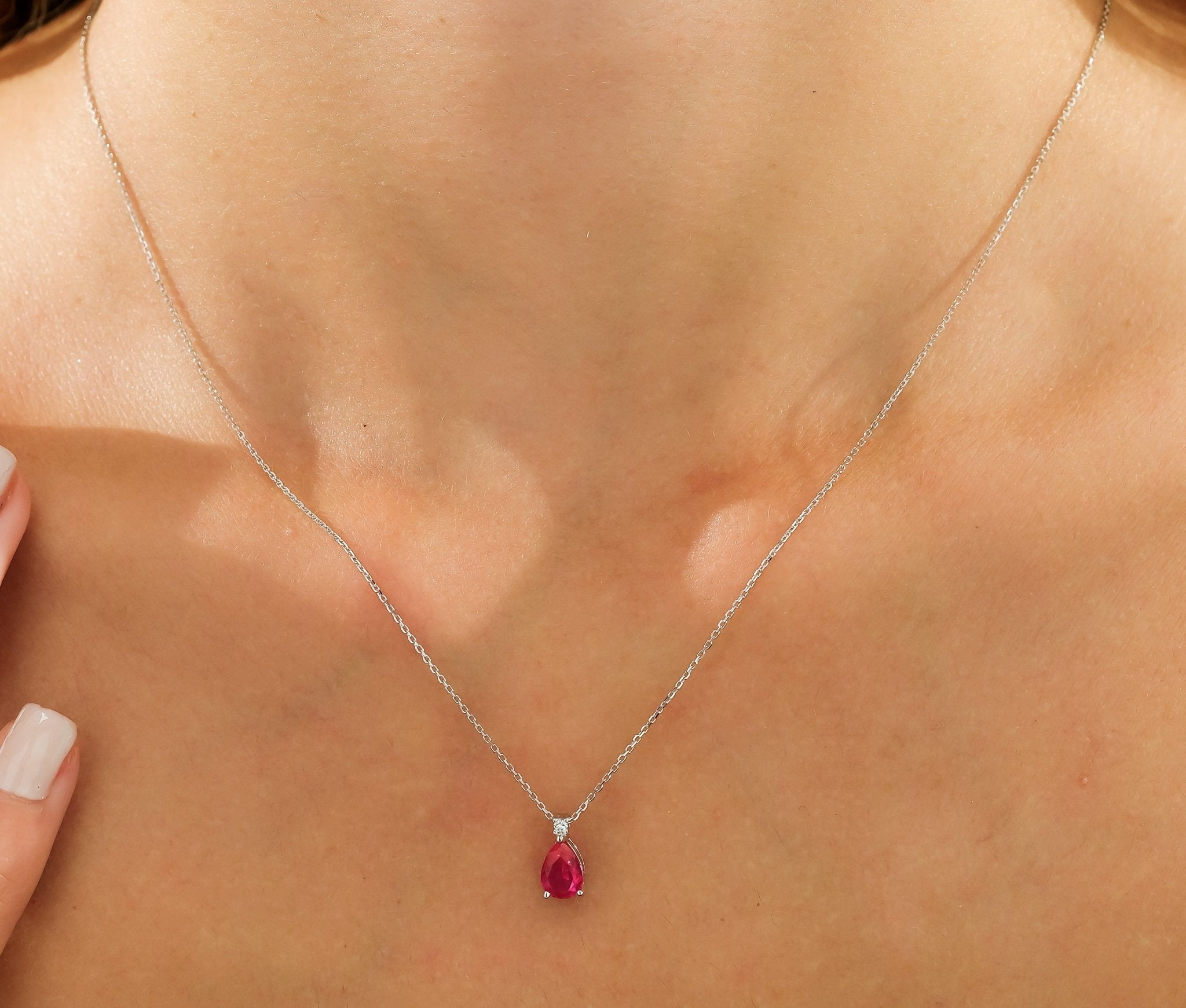 14K white gold necklace with pear shape ruby pendant and diamond accent, elegantly displayed on a woman's neck.