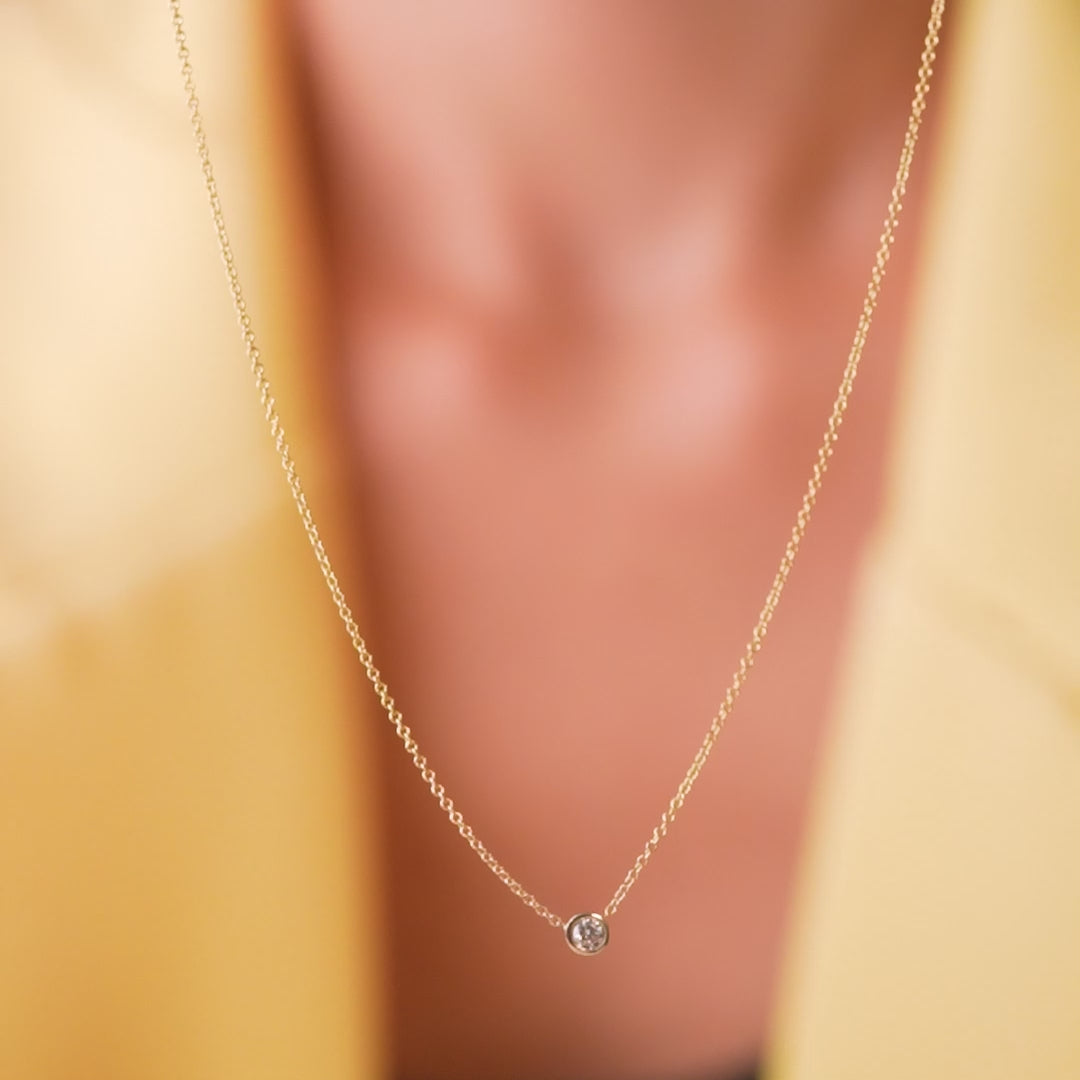 14K solid yellow gold minimalist diamond solitaire necklace on display, featuring a natural diamond in a bezel setting.