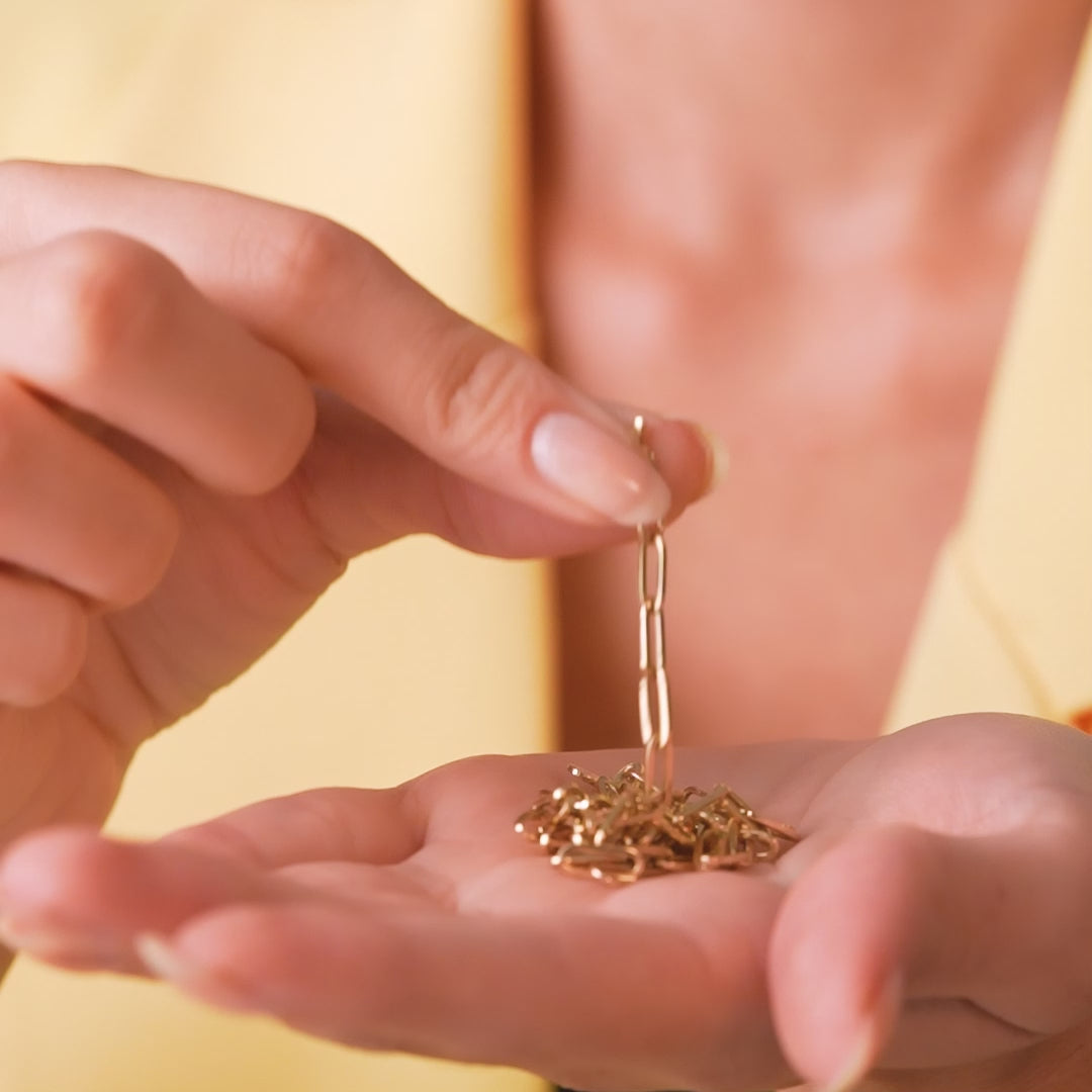 Woman holding a delicate 14K yellow gold paperclip necklace links in her hand, showcasing elegant jewelry.