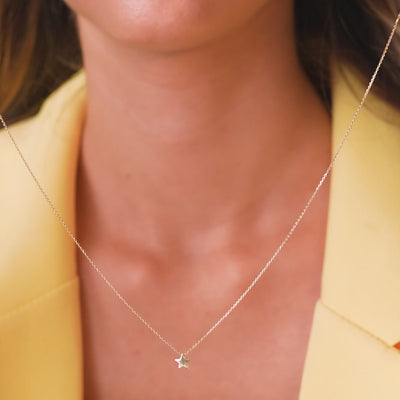 Dainty 14K solid yellow gold minimalist star necklace worn on a woman with a stylish outfit.