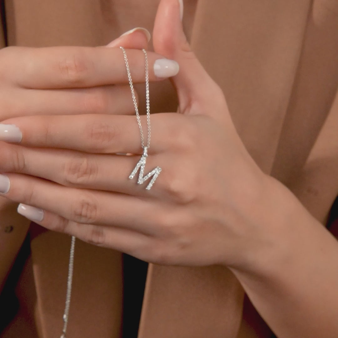 Hand holding a sparkling 14K white gold initial necklace with a diamond-studded letter M.