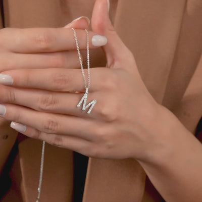 Hand holding a sparkling 14K white gold initial necklace with a diamond-studded letter M.