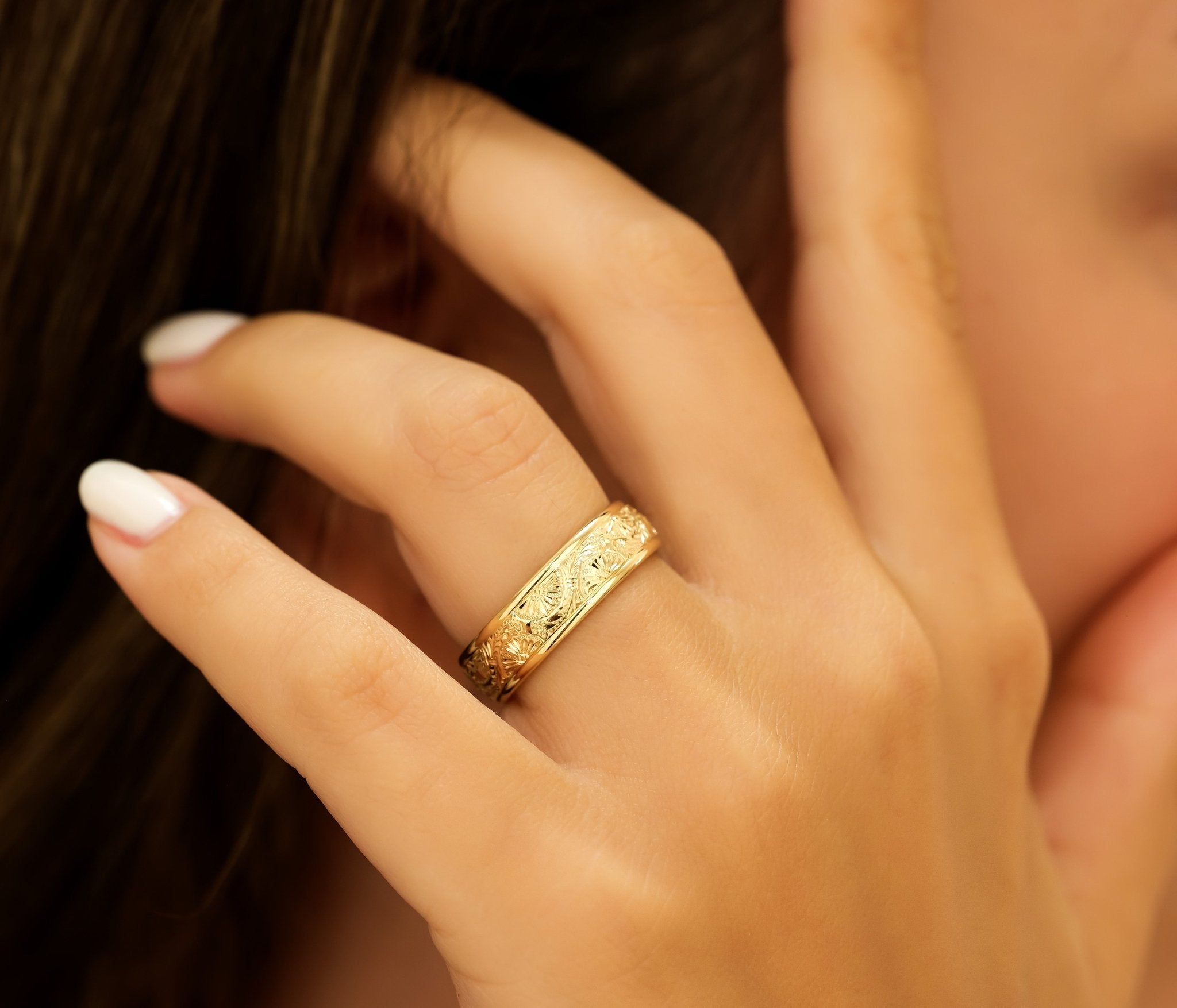 Woman wearing a 6mm yellow gold hand engraved wedding band with leaf motifs on her finger.